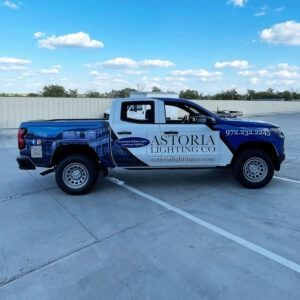 Blue-and-white Astoria Landscaping pickup truck parked on a concrete lot under a clear sky