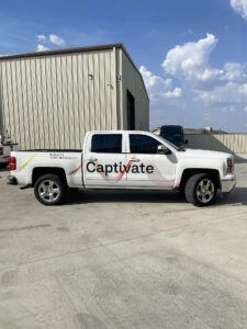 White Captivate pickup truck parked beside a beige metal building under a blue sky
