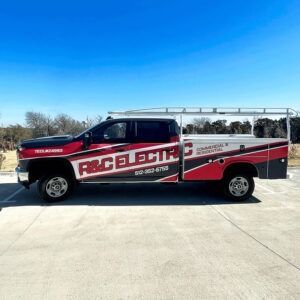 Red and black service truck with ladder racks parked on a concrete lot under a blue sky