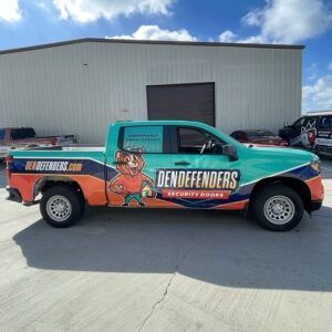 Teal and orange Dendefenders security truck parked in front of a warehouse