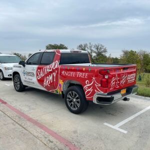 Red and silver Salvation Army pickup truck parked in a lot, with “Angel Tree” holiday graphics on the side.