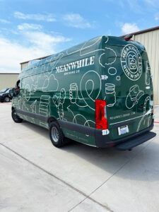 Green delivery van with white line art parked on a concrete lot under a blue sky