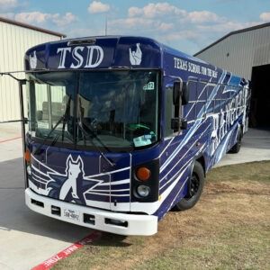 Purple Team Zombie Bus parked outside a warehouse, with wolf logo and TSD lettering on the front.