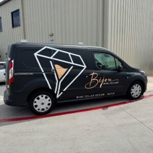 Black delivery van with a white diamond logo and “Bijen” branding parked beside a beige building.