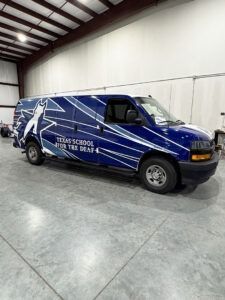 Blue branded van parked indoors in a warehouse, with white star graphics and school lettering.