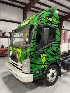 Green custom semi-truck cab with black graphics parked inside a warehouse, front-left view.