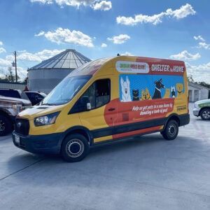Yellow pet grooming van with cat and dog graphics parked in a lot under a blue sky