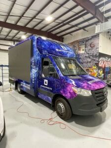 Purple-and-blue wrapped delivery van parked inside a warehouse garage