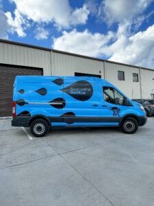 Blue wrapped cargo van parked outside a warehouse under a cloudy sky