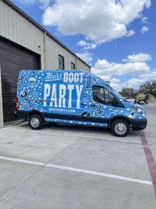 Blue “BOOT PARTY” van parked outside a warehouse under a partly cloudy sky.