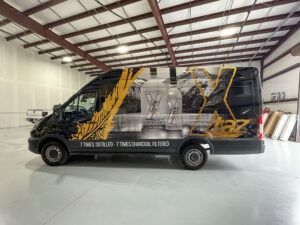 Black branded van with yellow graphics parked inside a large warehouse.
