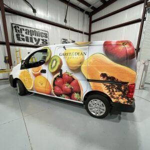Fruit-themed delivery van wrap in a warehouse, with bright images of oranges, kiwis, strawberries, and papaya.