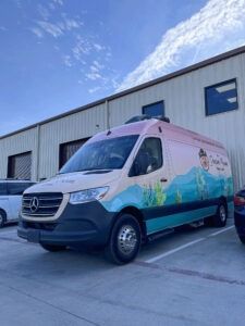 Pink and blue Mercedes van parked outside an industrial building under a blue sky