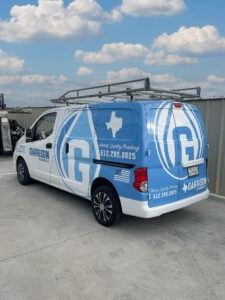 Blue-and-white utility van with Texas logo and ladder rack parked on a concrete lot under a cloudy sky
