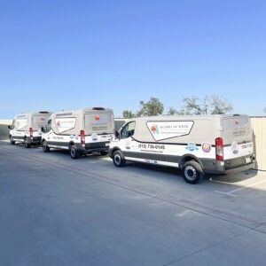 Three white service vans parked in a row on a sunlit paved lot.