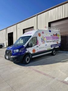 Delivery van parked outside warehouse building with purple and white branding on the side