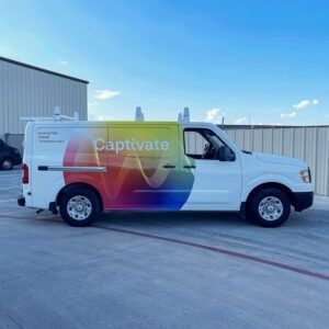 White Captivate van parked on a lot with a colorful rainbow graphic on the side under a blue sky