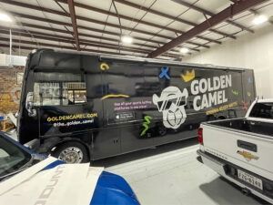 Golden Camel branded tour bus parked indoors beside a white pickup truck