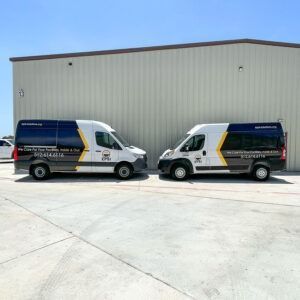 Two white-and-blue delivery vans parked nose-to-nose in front of a large warehouse.