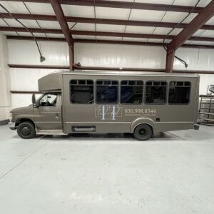Gray shuttle bus parked inside a warehouse with red steel beams and a white floor