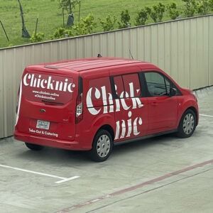 Red delivery van with “Chicknic” branding parked in a lot beside a fence