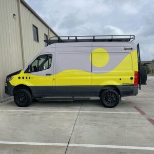 White cargo van with bright yellow and black wrap parked beside a building.