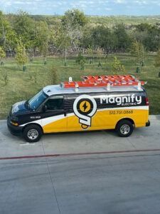 White and yellow Magnify service van with ladder on roof driving beside a road and grassy field.