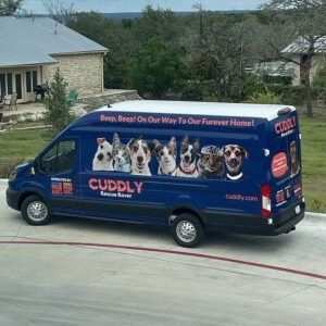 Blue Cuddly animal rescue van with dog photos parked on a residential street near houses