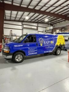 Blue Raptor-branded service van parked inside an auto shop with white floor and metal ceiling