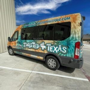 Colorful Twisted Texas van parked beside a warehouse under a bright blue sky