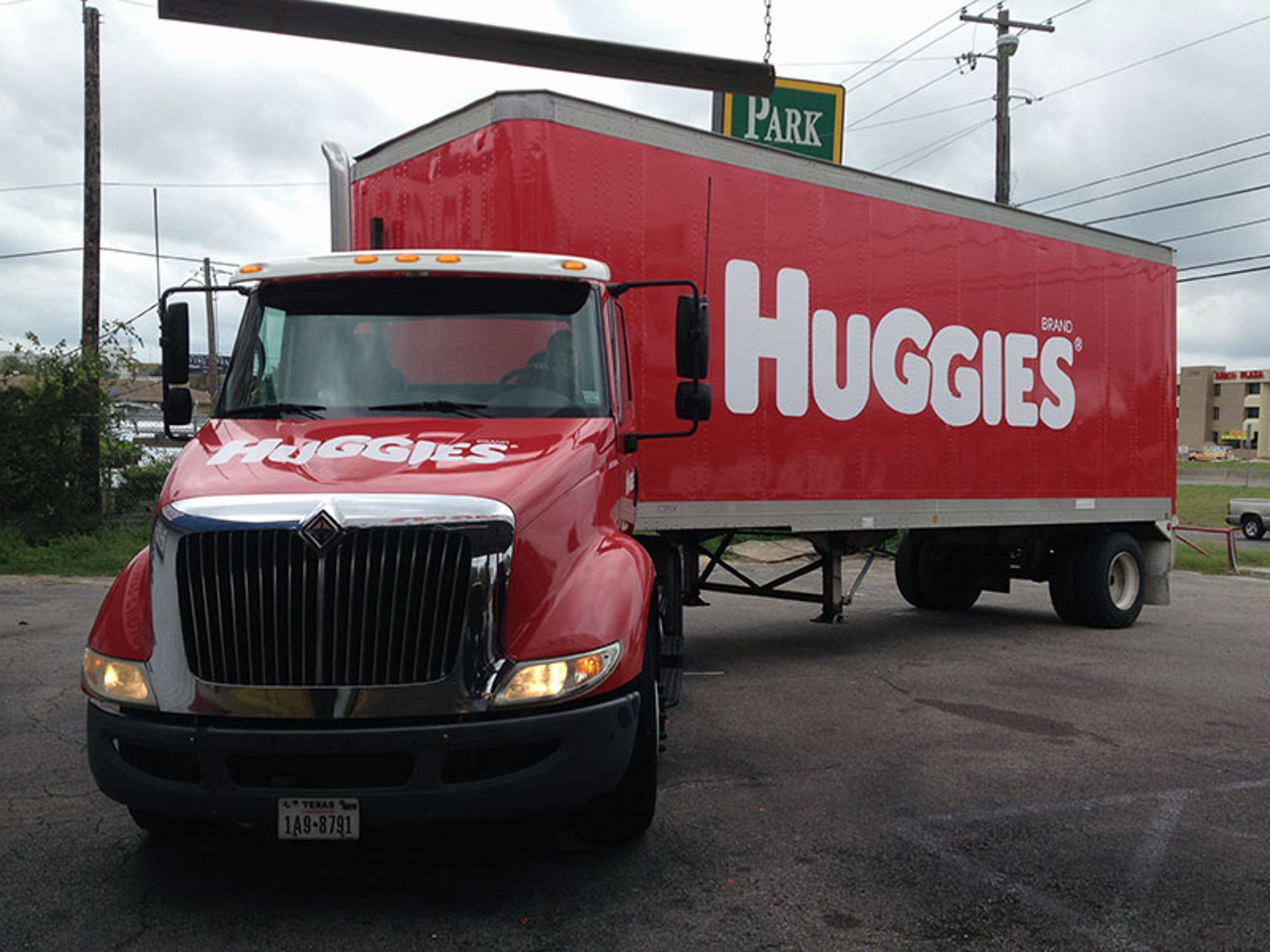 Red Huggies delivery truck parked on a wet lot under an overcast sky