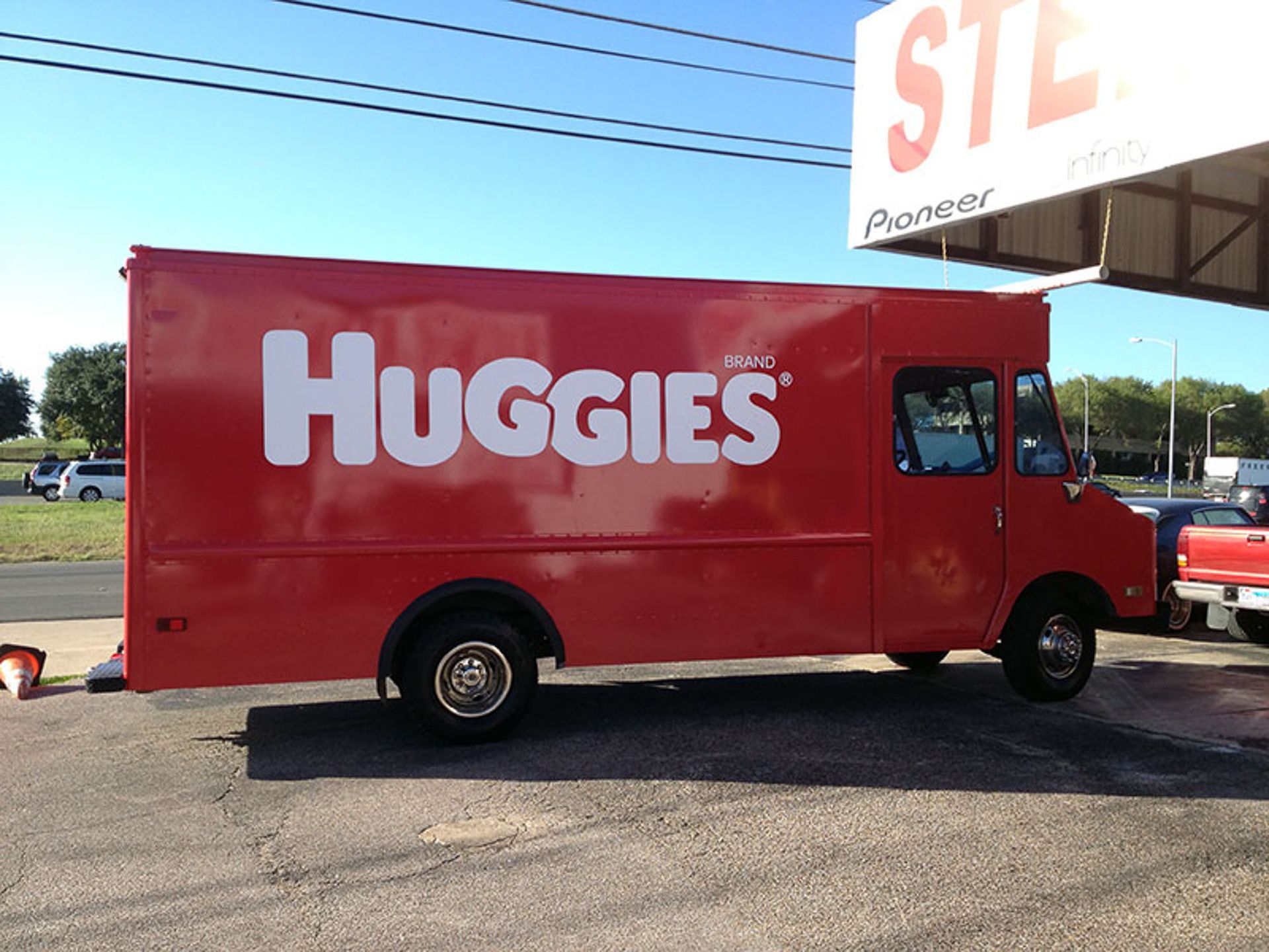 Red Huggies delivery truck parked outside a store on a sunny day