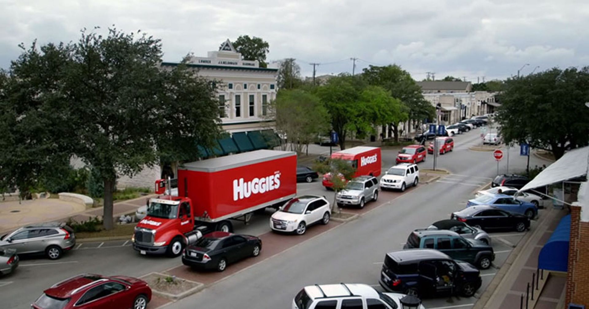 Street with red delivery trucks and parked cars near a row of buildings on an overcast day