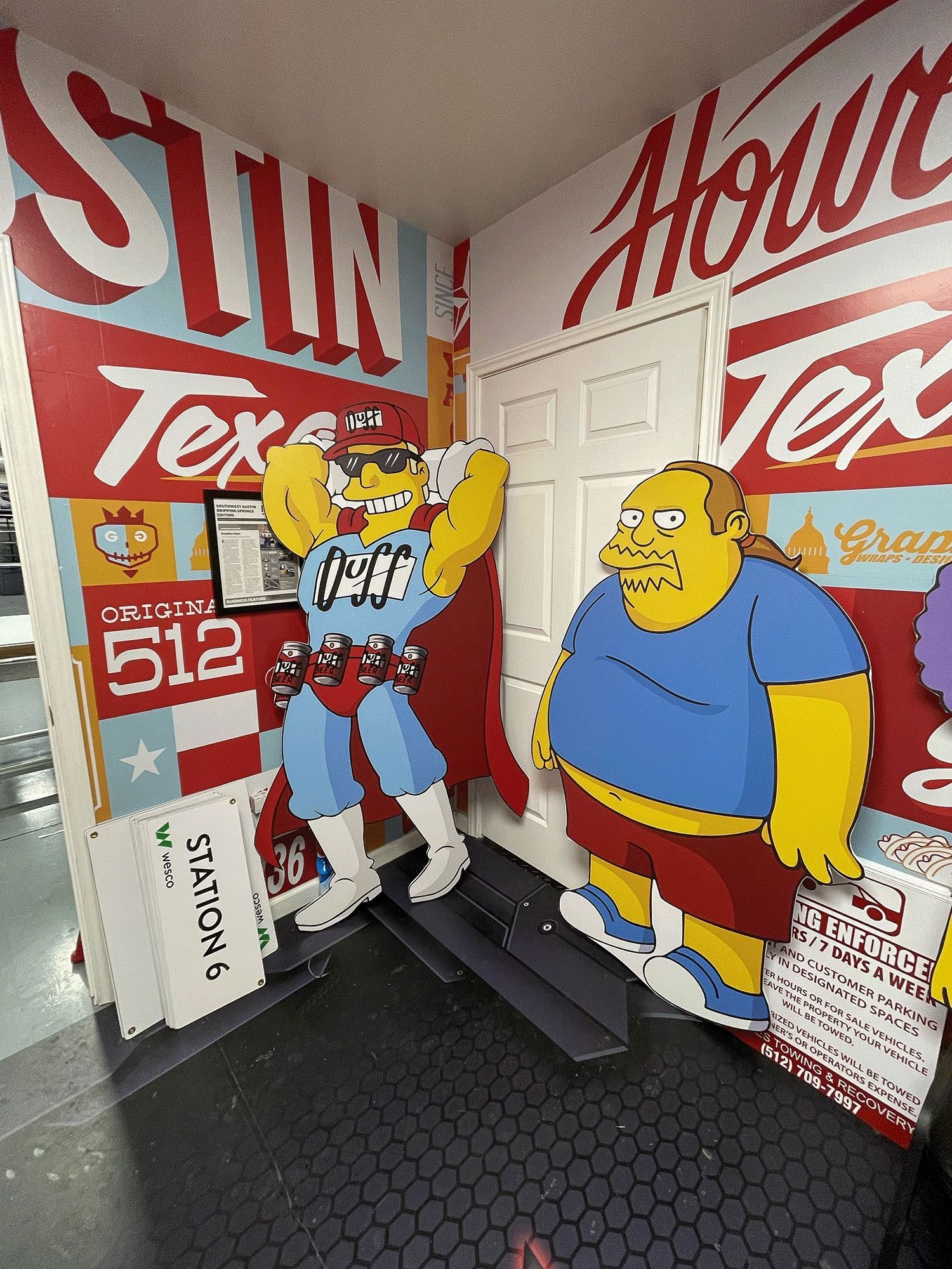 Simpsons-themed room with large wall art, Bart and Homer cutouts, and a white door on a black floor