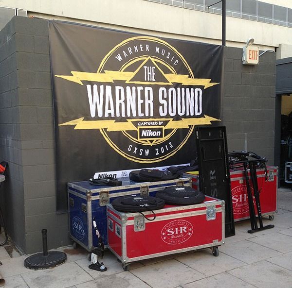DJ booth with Warner Sound banner, turntables, and red equipment cases in an outdoor alley