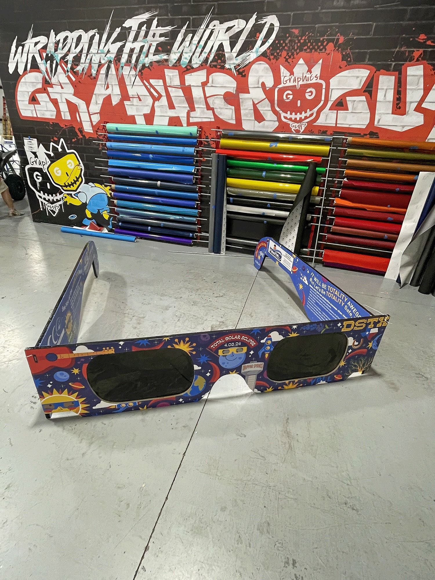 Graffiti-style arcade game setup with colorful metal rails and a wall of stacked pipes in a warehouse-like space