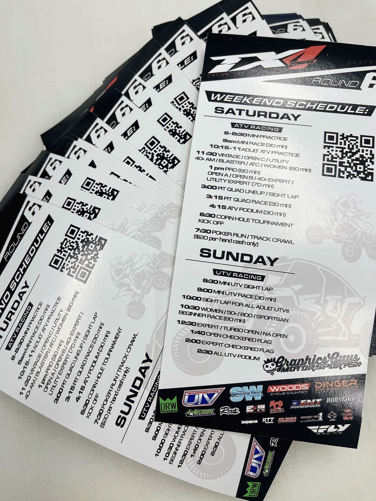 Stack of black-and-white event flyers with QR codes, fanned out on a white surface.