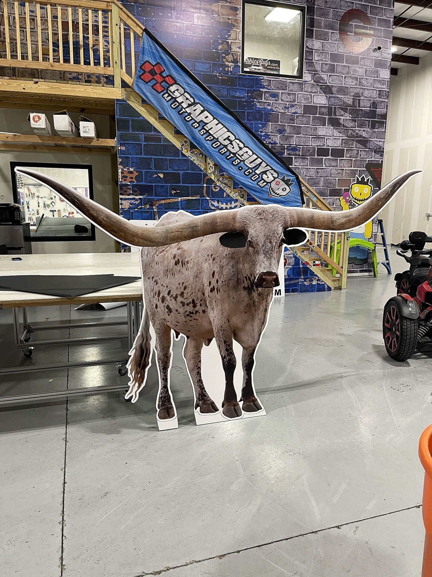 Longhorn cow statue indoors on a polished floor, with a blue brick wall and staircase behind it
