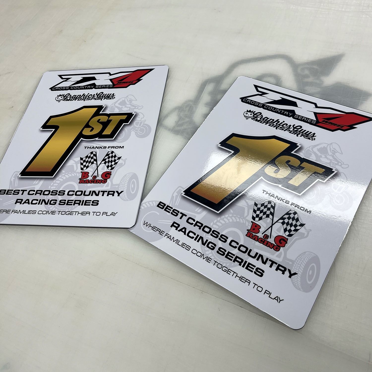 Two glossy first-place racing country series award plaques on a white surface, one standing in shadow