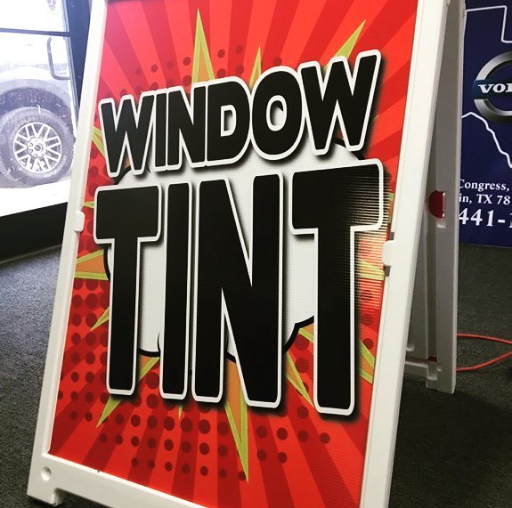 Red and orange sign reading “WINDOW TINT” on a sidewalk display stand