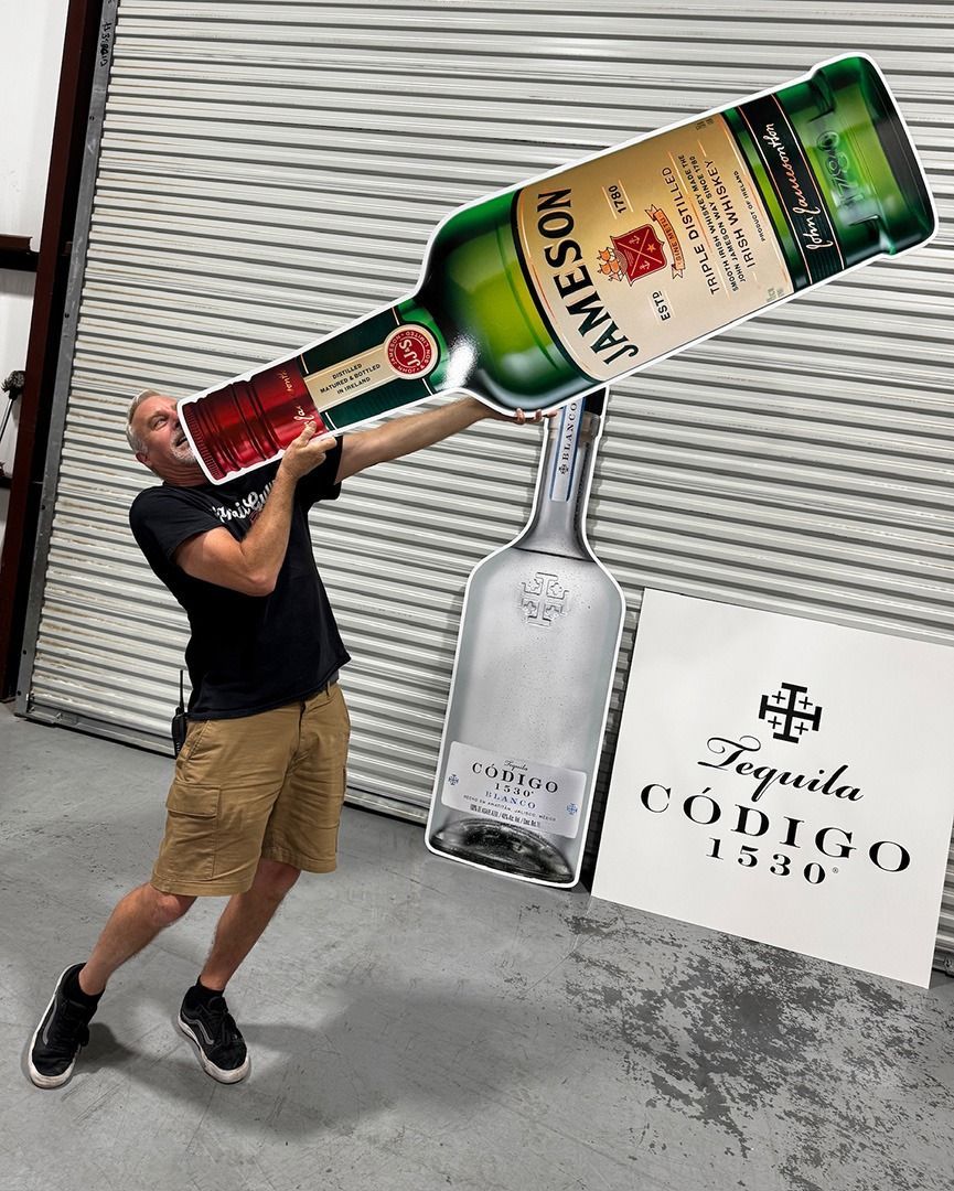 Person posing with a giant Cointreau bottle prop in front of a liquor store shutter.