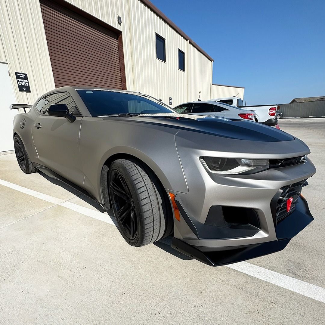 Matte gray sports car parked outside an industrial building in bright sunlight.