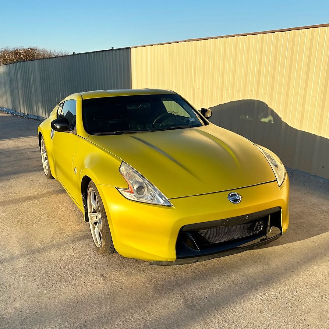 Yellow sports car parked on pavement beside a beige wall in warm sunlight
