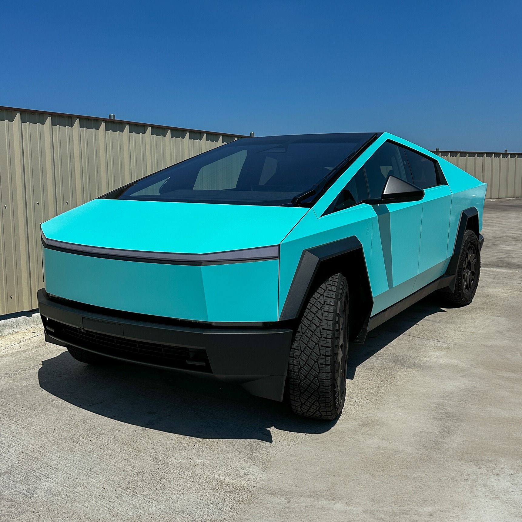 Bright turquoise and black Tesla Cybertruck parked outdoors in sunlight.
