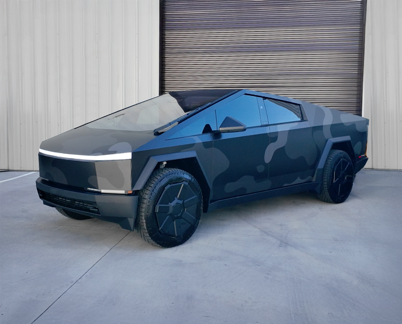 Blue camouflage Tesla Cybertruck parked outside a garage door.