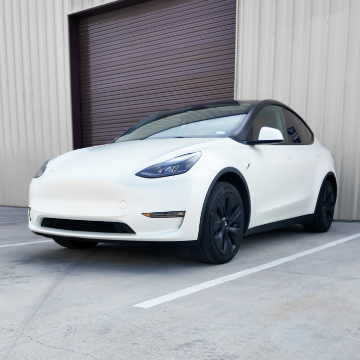 White Tesla Model Y parked outside a warehouse with a brown roll-up door