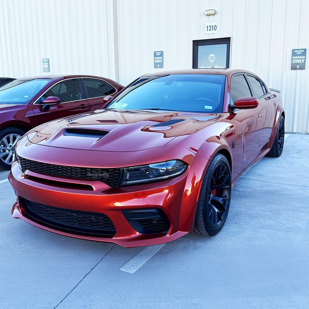 Red Dodge Charger parked outside a building, front view with black rims and a hood scoop