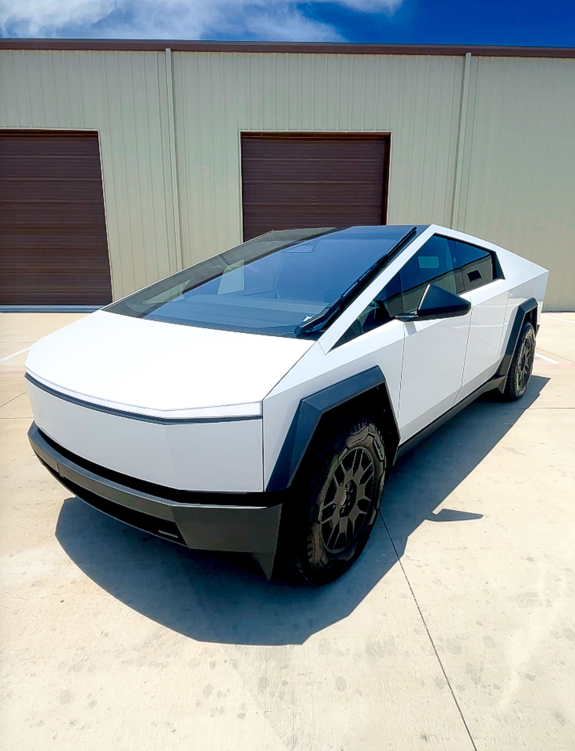 White Tesla Cybertruck parked outside a warehouse on a sunny day