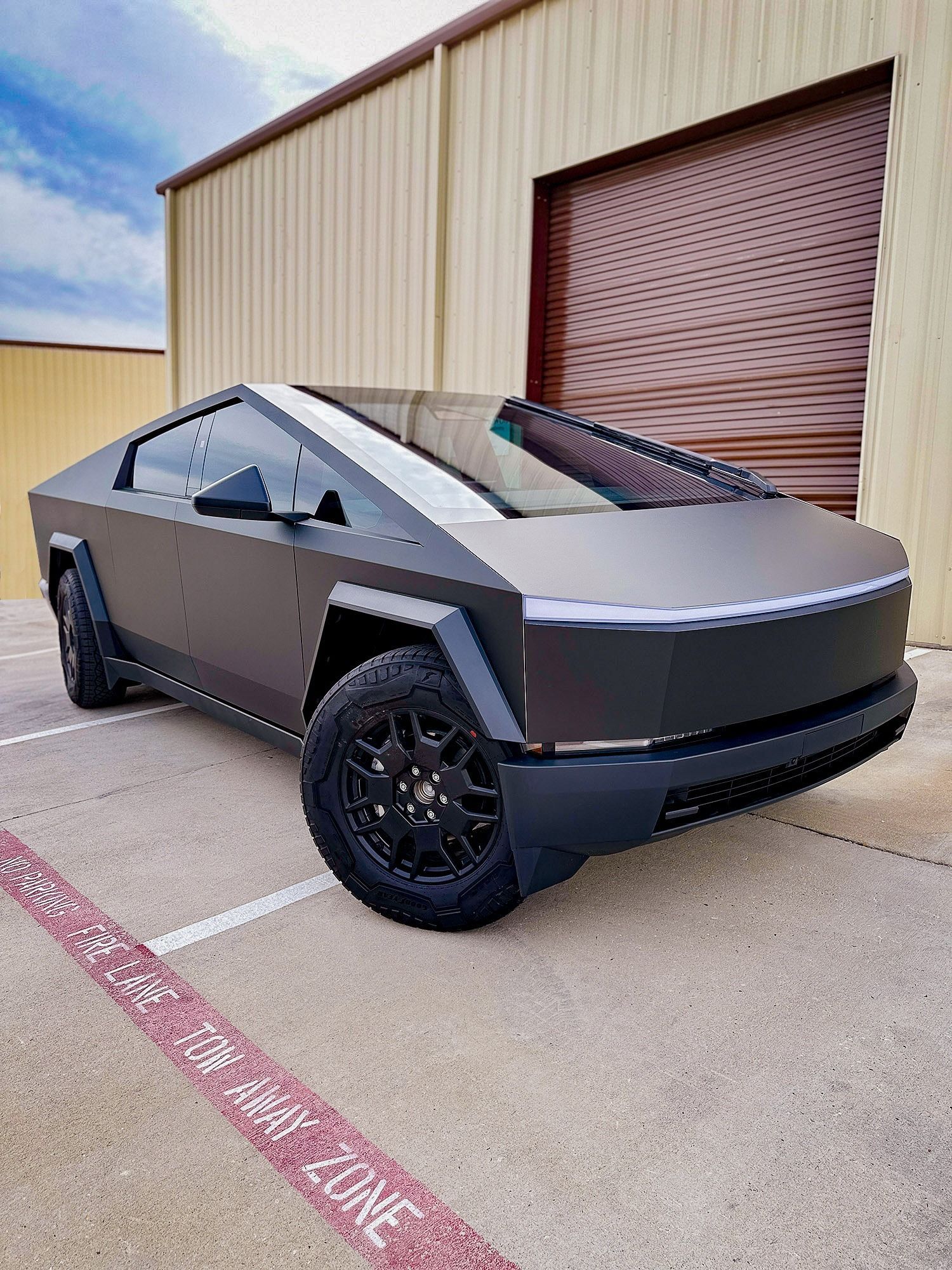 Gray futuristic pickup-style electric truck parked beside a tan industrial building.