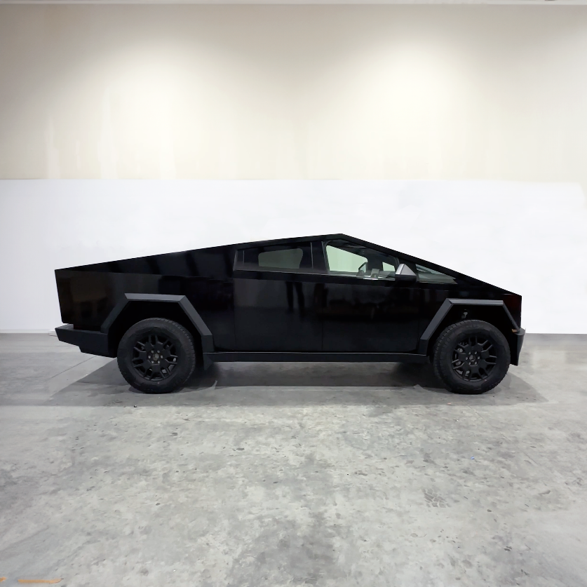 Black angular pickup truck in side view, parked indoors against a white wall.
